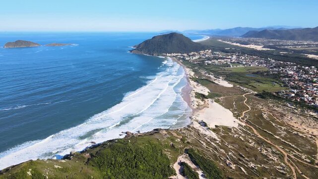 Panoramic aerial view of Santinho beach and Aranhas Island, restinga area and dunes seen from the top of Ingleses hill on a beautiful sunny summer day.