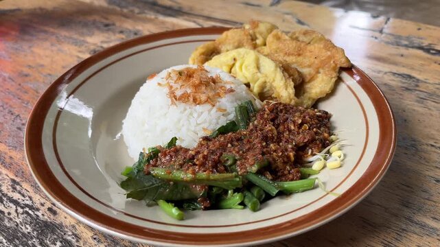 Nasi pecel or sega pecel is a typical Javanese Indonesian rice dish served with pecel. spicy hot peanuts sauce, vegetables and fried chicken egg. Wooden table. Close up view.