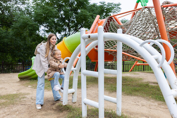 Mother helping young daughter climb playground equipment at a park