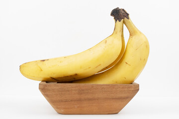 Two whole yellow bananas rest in a small wooden bowl isolated against a clean white background.