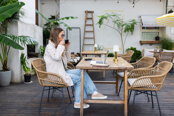 Young woman working on a laptop and drinking coffee at an outdoor cafe