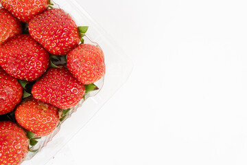 Fresh red strawberries fill the left side of a clear plastic container with white copy space on the right.