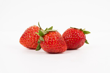 Small group of three berries displays fresh red strawberries with vibrant green stems isolated on white.