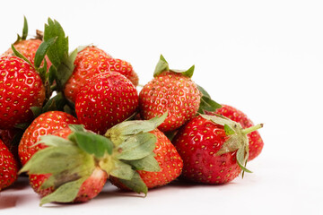 Close up heap of fresh berries shows red strawberries piled against a bright white background.