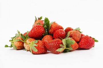 Pile of bright red strawberries rests in a heap showing fresh green leaves isolated on white.