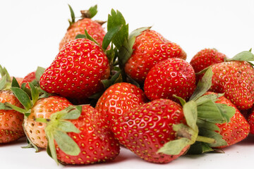 Close up pile of fresh berries shows red strawberries densely packed against a bright white background.