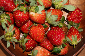 Close up pile of berries fills a dark wooden bowl showing fresh red strawberries ready for eating.