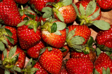 Macro close up image of fresh red strawberries shows texture and green stems in a dense arrangement.