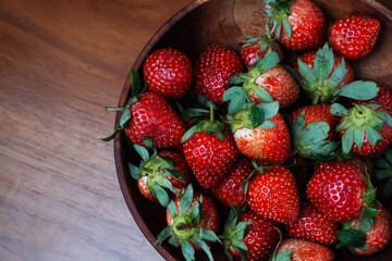 Wooden bowl of fresh strawberries occupies the right side against a warm wood background.
