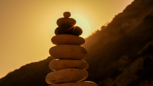 Balance cairn sunset silhouette of stacked stones against a dark mountain hillside during peaceful golden hour.