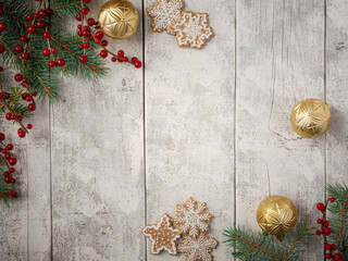 Evergreen pine spruce branch needles greenery pinecones and red berries on white rustic wood plank table with gold ornaments and cookies. Winter festive Christmas holiday seasonal overhead flatlay