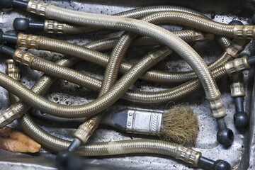 Messy pile of old, dirty, braided metal hose and flexible pipe with brush in steel tray at workshop, suggesting industrial maintenance and repair work
