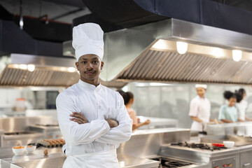 Confident male chef in white uniform standing with arms crossed in modern kitchen. Concept of culinary leadership, career in food service, professionalism and kitchen authority.