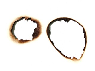 Close up of a fire burned hole on white paper background. Black burn mark and paper stain texture detail. A piece of scorched and torn paper with a fire burned hole and black scorch marks with stain.