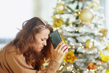A woman with her eyes closed, forehead leaning on her smartphone, appears distressed in profile...
