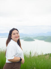 Confident curvy Asian woman smiling in nature with lake and mountain background.