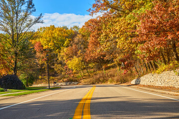 Country road with yellow line going down the middle and colorful fall leaves on a pretty autumn day