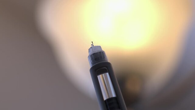 Small drops of medical drug drip out of needle tip of injection pen
