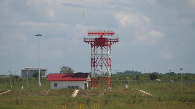 Red and white airport radar tower with adjacent building in grassy surroundings at KTI International Airport, Phnom Penh, Cambodia. Aerial navigation and communication systems