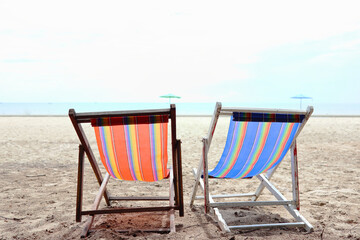 Two chairs are placed on the sandy beach, overlooking the clear sky and sea.