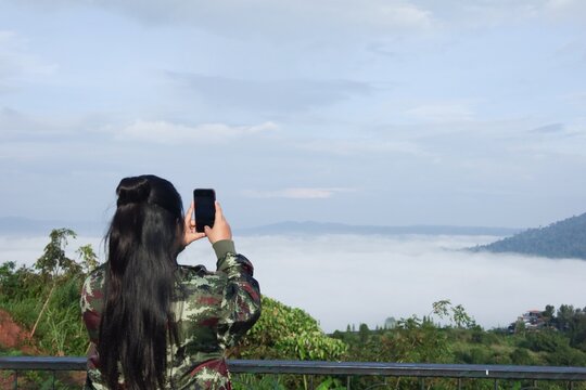 Rear view of a young female tourist using her smartphone to take a photo of the mountain view.