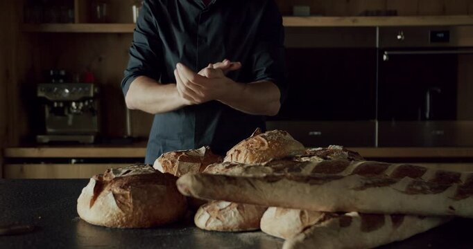 Man in black shirt in Modern and spacious wooden kitchen room cut a round bread on table. Real Estate. Luxury kitchen with island and chairs. Minimalist design in New Home.