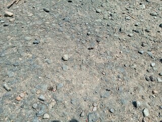 Closeup Texture of Rough Asphalt Road Surface with Small Stones and Dust in Sunlight