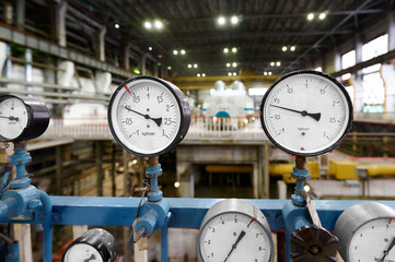 Analog pressure gauge displays measurements in industrial environment with equipment and lighting in background