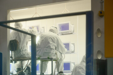 Workers engaged in powder coating process in controlled environment with equipment and monitors present