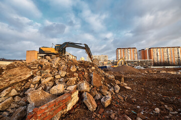 Bucket of excavator digs leftovers of destroyed building