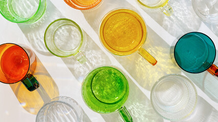 Colored Glasses summer pattern with shadow and sunlight reflection on white, minimal aesthetic top view banner, refraction at shine drink, caustic effect, close up green orange yellow glass cups