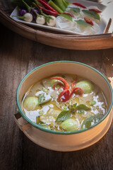 Authentic Thai green curry with tender chicken and eggplants served with rice noodles and fresh vegetables. Traditional Thai food still life on wooden table, beautifully arranged with basil leaves