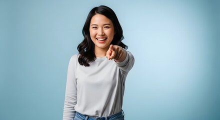 Fototapeta premium Smiling Asian woman pointing at camera on blue background, cheerful young Asian female showing positive emotion and confidence gesture, casual outfit studio portrait, Asia women lifestyle concept