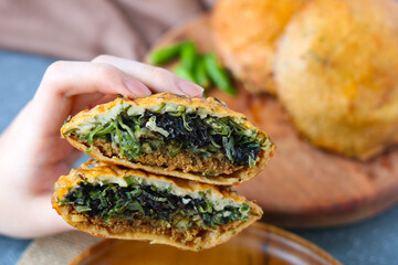Hand holding an Ote-Ote Porong or oyster cake that is cut in half, revealing a savory filling of oysters, meat and green onions. In the background are green chilies (cabe rawit).