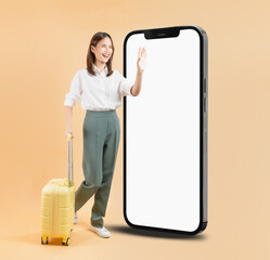 Happy Asian business woman holding suitcase and hand touching a large smartphone screen isolated on beige color background, travel concept.