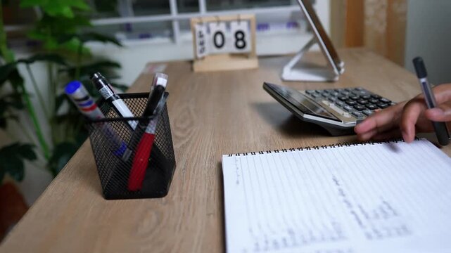 Person using a calculator and writing in a notebook on a desk