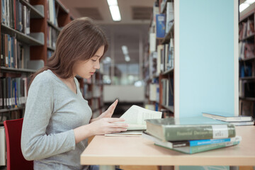 A teenage girl sitting on the table of a library, searching information