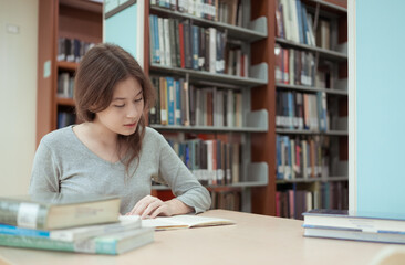A teenage girl sitting on the table of a library, searching information