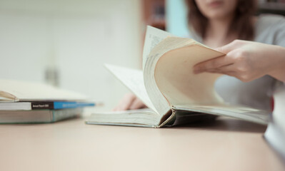 A teenage girl sitting on the table of a library, searching information