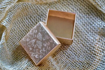 Empty floral gold box with open lid, placed diagonally on a golden surface—luxury packaging with elegant depth