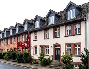 Fototapeta premium Row of houses with windows and dormers, one with red ivy creeping up the wall; a street in front on lower left