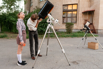 Man observes sky using telescope during astronomy session. A man in a white shirt looks through a telescope during an outdoor astronomy session, carefully adjusting the instrument to observe celestial