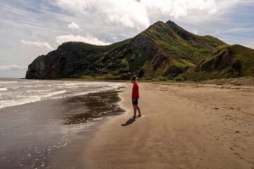 Girl in red jacket standing on sandy beach near mountains