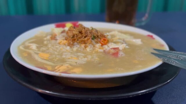 Bowl of hot noodle soup with light steam rising, topped with crispy fried shallots and colorful garnish.