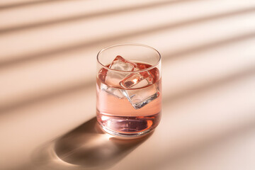 Glass of pink liquid with ice cubes and striped shadows drink refreshment