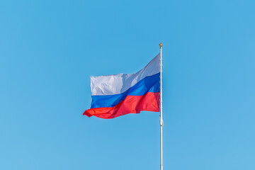 Russian tricolor flag waving in the wind against a blue sky.