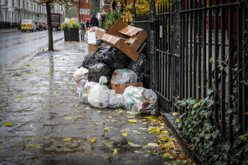 Stack of garbage bags and cardboard boxes on a rainy urban street. Waste management, pollution, and environmental issues