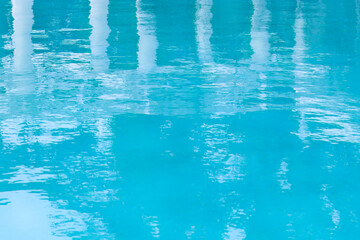 Turquoise outdoor pool with reflection of snow-white columns. Abstract water surface with ripples. Blue texture background. Summer vacation concept.