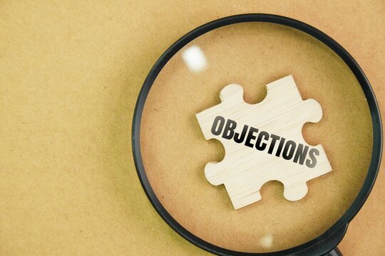 Magnifying glass and wooden puzzle with the word Objections. a reason or argument offered in disagreement, opposition, refusal, or disapproval