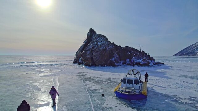 Tourists walk on the frozen surface of Lake Baikal. A hovercraft carries tourists across the ice. Winter travel.